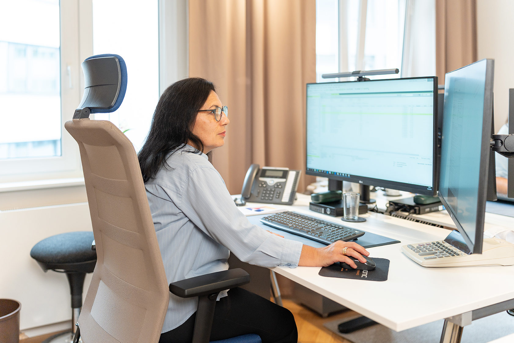 Mitarbeiterin der Rose Treuhand GmbH arbeitet konzentriert an zwei Monitoren in einem modernen Büro.