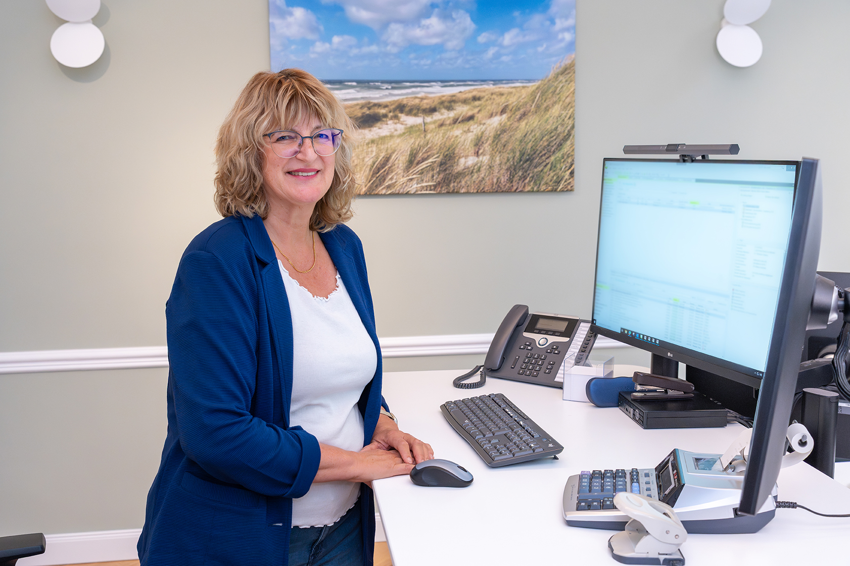 Mitarbeiterin der Rose Treuhand GmbH steht an ihrem höhenverstellbaren Schreibtisch und arbeitet am Computer.